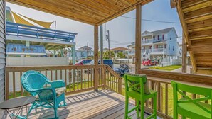 A wooden deck with two rocking chairs and a small table, overlooking a residential street with houses and parked cars.