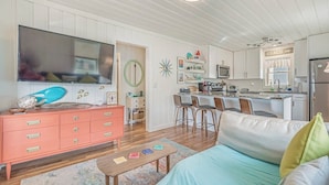 A modern living room with a sofa, coffee table, and a television. There is a kitchen area with a microwave and a refrigerator. - Coconut Flats Duplex- Upstairs- (North Myrtle Beach)