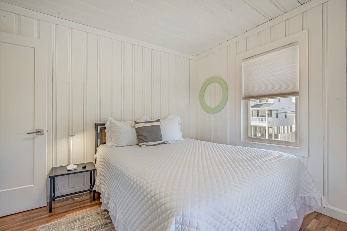 Un dormitorio con cama, mesita de noche, lámpara, ventana con persianas y puerta.