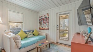 A cozy living room with a white sofa, colorful cushions, a coffee table, and a large window with blinds. - Coconut Flats Duplex- Upstairs- (North Myrtle Beach)