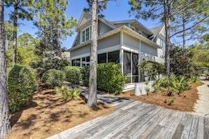 A two-story house with a covered porch, surrounded by pine trees and a wooden deck. - 🌴 Moon Landing • Luxury WaterSound West Retreat with LSV, Bikes & Pool Access (30A WaterSound)