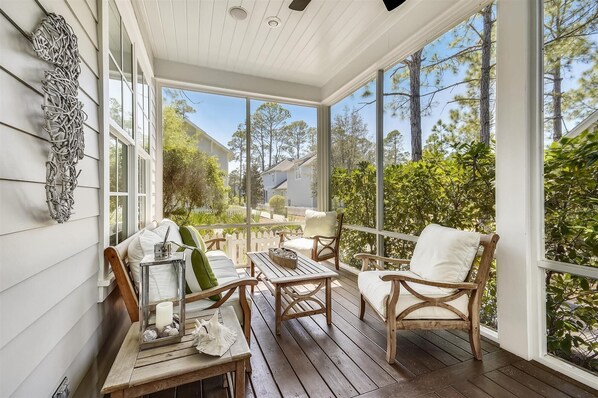 A covered porch with wooden furniture, a table, and a decorative wall piece.