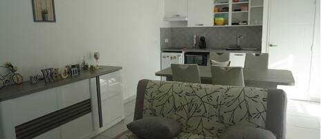 Una cucina moderna con mobili bianchi, un'area pranzo con tavolo e sedie grigie e un divano con motivo a foglia.