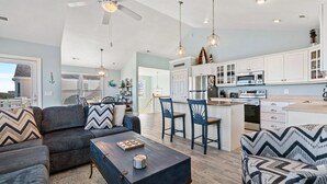 A modern kitchen with white cabinets, a microwave, and a refrigerator. There is a dining area with two chairs and a table. - Beachin Up With The Jones's: Private Pool, Dogs OK (Corolla)