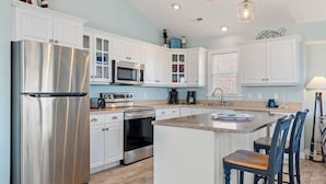 A modern kitchen with white cabinets, stainless steel appliances, and a central island with bar stools. - Beachin Up With The Jones's: Private Pool, Dogs OK (Corolla)