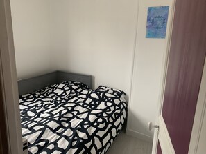Una habitación pequeña con una cama individual, colcha estampada, cabecera y una puerta con manija.