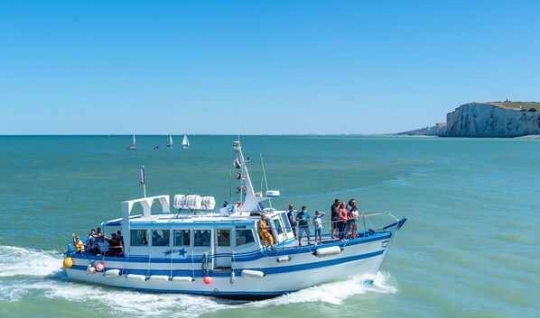 Un barco con pasajeros navegando por aguas tranquilas cerca de una costa con acantilados.