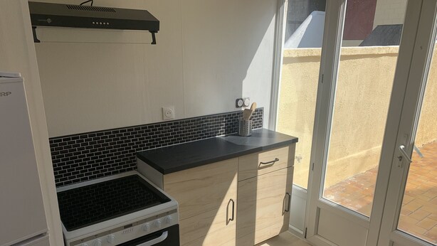 Une cuisine compacte avec un dosseret carrelé en noir et blanc, une cuisinière et un plan de travail noir.