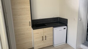 Une cuisine de taille réduite, équipée d’un lave-vaisselle, de meubles en bois et d’un plan de travail noir.