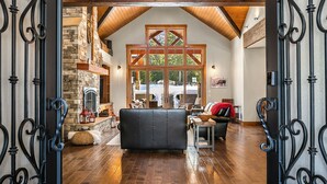 A spacious living area with a stone fireplace, wooden beams, and a large window overlooking a snowy landscape. - Private Indoor Pool! The Northwest's most unique vacation experience!! (Cle Elum)