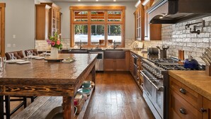 A modern kitchen with a central island, wooden cabinetry, a large stove, and a view of the outdoors through a large window. - Private Indoor Pool! The Northwest's most unique vacation experience!! (Cle Elum)