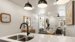 Une cuisine moderne dotée d’un évier à deux bacs, de luminaires suspendus, d’un coin repas avec une table dressée pour deux personnes et d’un grand miroir.