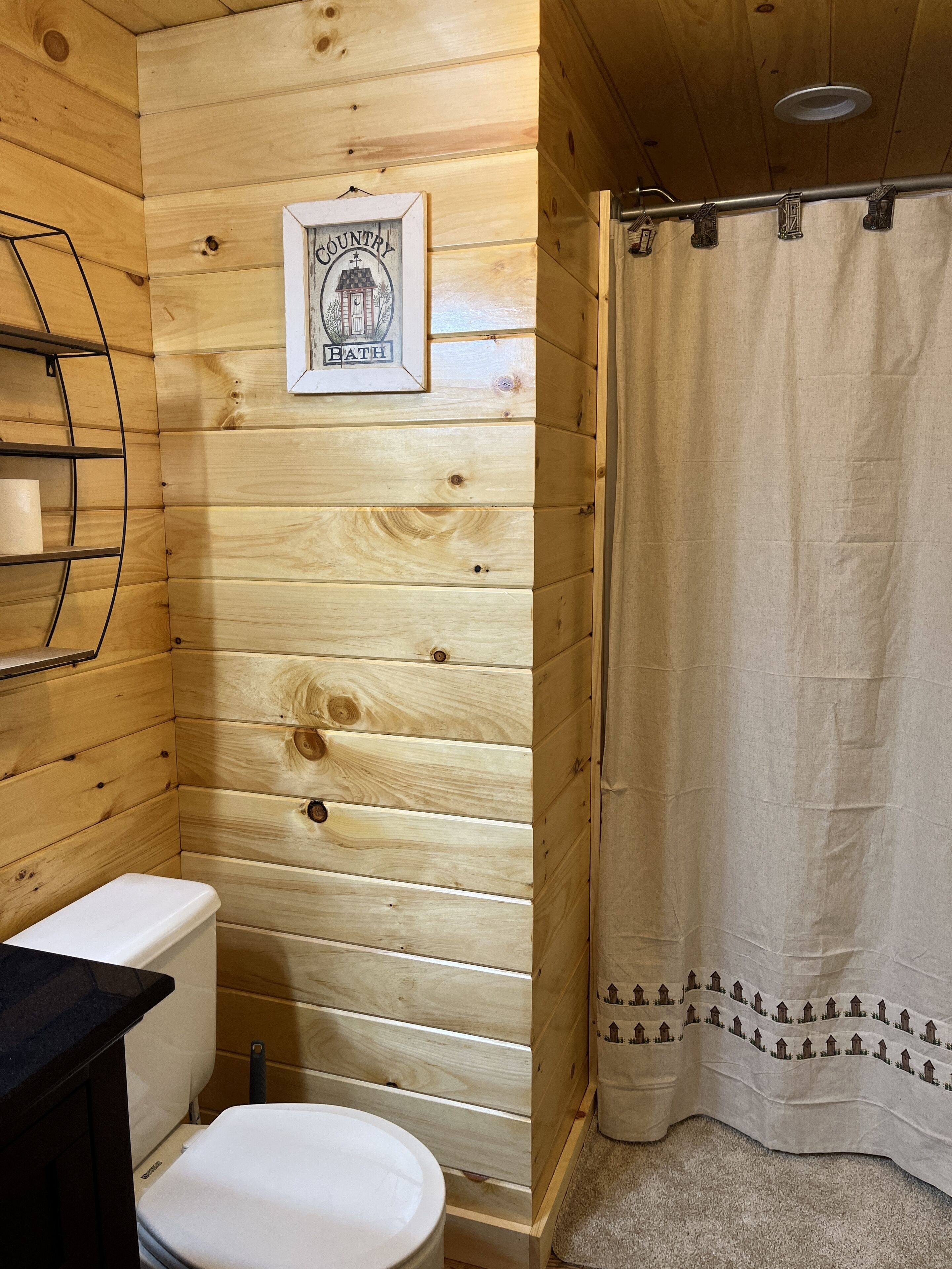 Ein Badezimmer mit Holzvertäfelung, einer Toilette, einem gerahmten Bild an der Wand und einer Duschvorhang.