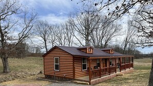 A log cabin with a porch and two windows, surrounded by trees and a gravel driveway. - Griffis Game Hunting and/or Getaway (West Union)