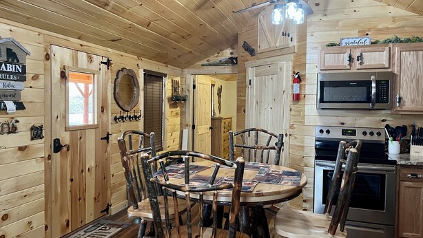 A cabin interior with a wooden interior, a dining table with chairs, a ceiling fan, a microwave, and an oven. - Griffis Game Hunting and/or Getaway (West Union)