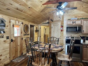 A cabin interior with a wooden dining table, chairs, a ceiling fan, a microwave, and an oven.