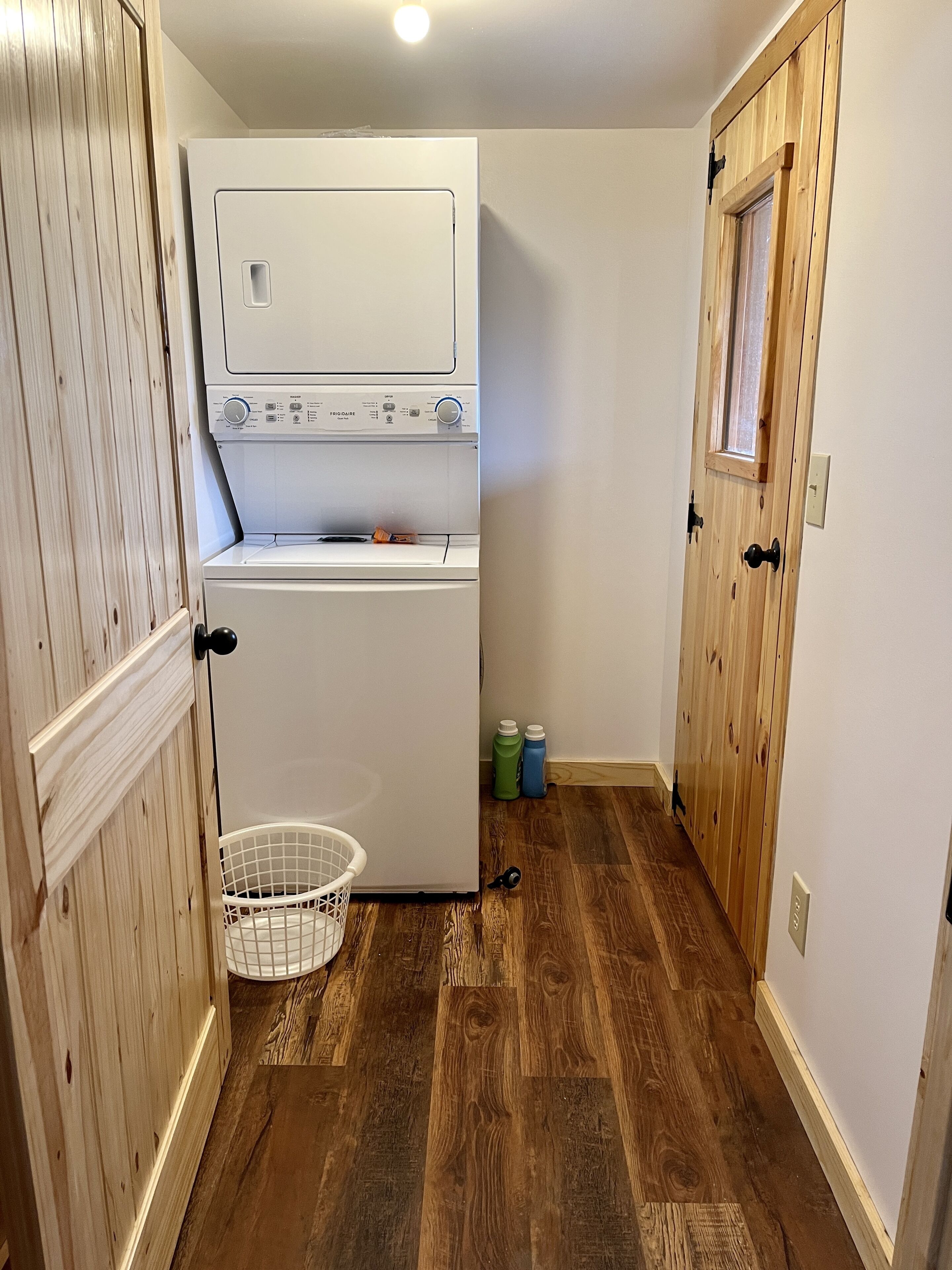 A laundry room with a front-loading washer and dryer, a wooden door, and a small window.