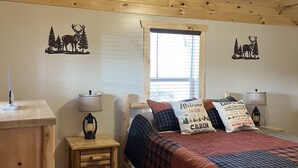 A wooden cabin bedroom with a bed, a nightstand, a lamp, and a ceiling fan. - Griffis Game Hunting and/or Getaway (West Union)