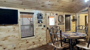 A cabin interior with a wooden interior, a round dining table with chairs, a mounted television, and a ceiling fan. - Griffis Game Hunting and/or Getaway (West Union)