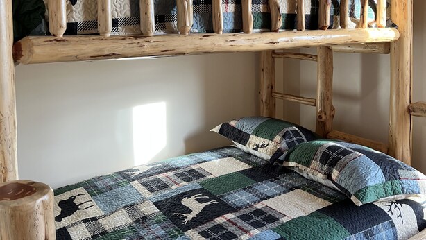 Un lit superposé avec une structure en bois et une couvre-lit matelassée ornée de motifs représentant des animaux.
