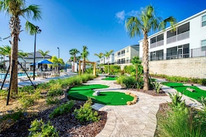 Un parcours de golf doté d’une piscine, de palmiers et d’un bâtiment avec des balcons.