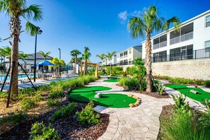 Un parcours de golf doté d’une piscine, de palmiers et d’un bâtiment avec des balcons.