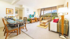 A modern living room with a dining area, a sofa, and a large window with a view. - 2BR Condo w/ lanai & Diamond Head views (Honolulu)