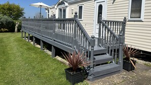 Een gelijkvloerse stacaravan met een voortuin, een kleine trap en een overdekt terras.