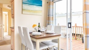 Een eetgedeelte met een tafel gedekt voor twee personen, een schilderij van een strand en een uitzicht op een balkon met een hekwerk.