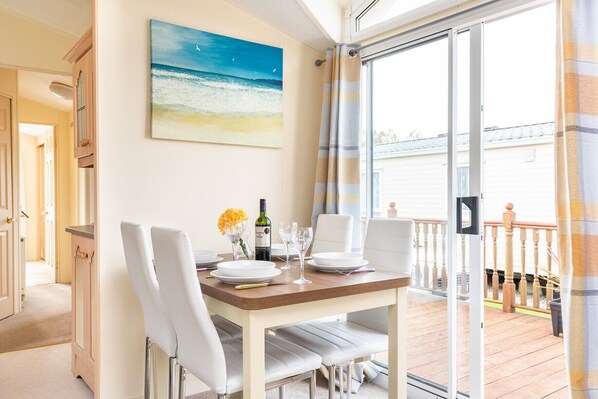 A dining area with a table set for two, a painting of a beach scene, and a view of a balcony with a railing.