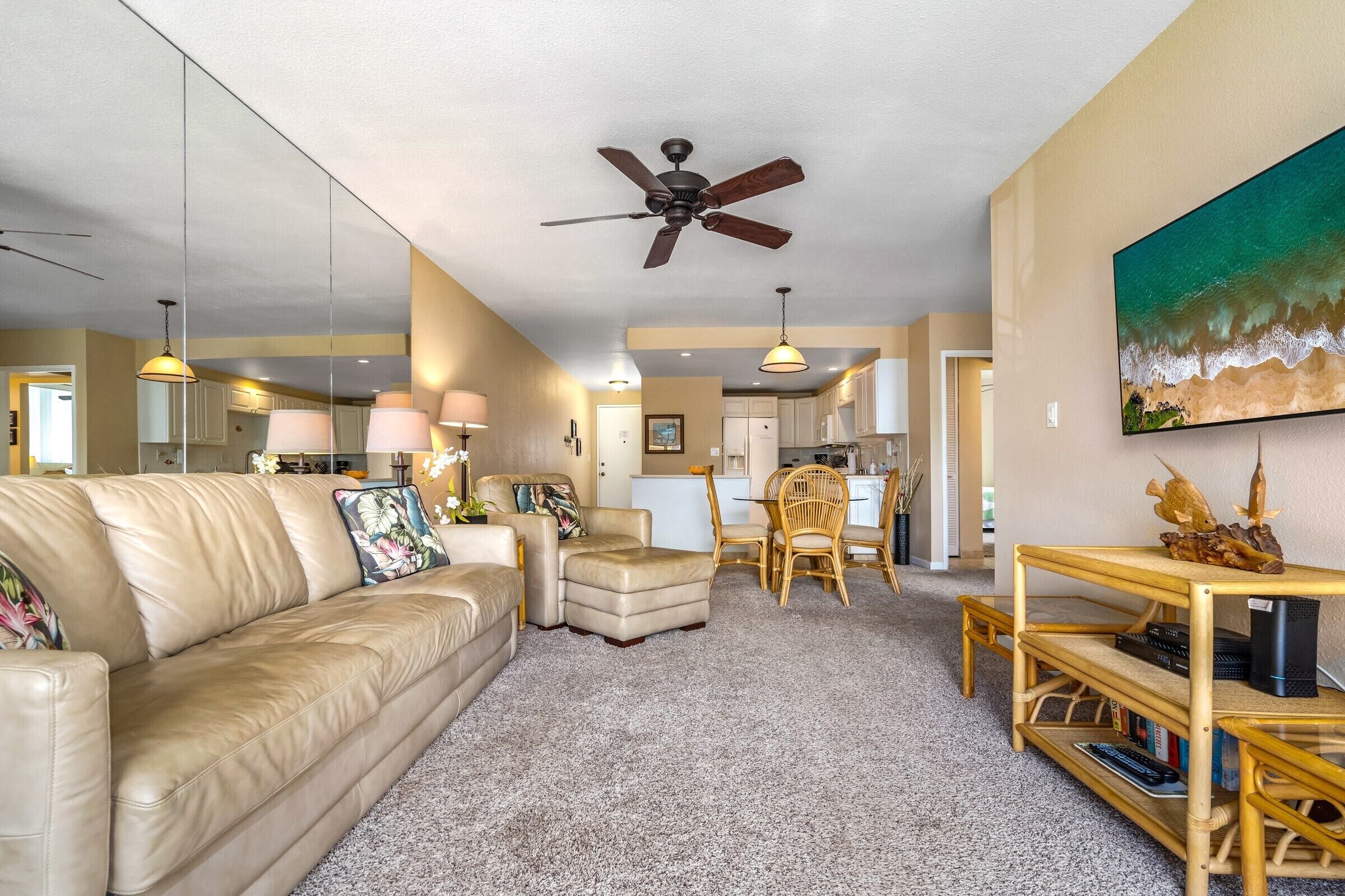 A spacious living room with a beige leather couch, a wooden coffee table, and a dining area with wicker chairs.