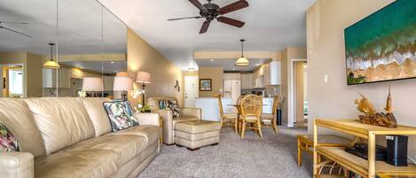 A spacious living room with a beige leather couch, a wooden coffee table, and a dining area with wicker chairs.