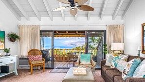 Ein Wohnzimmer mit Meerblick, einem Deckenventilator, einem weißen Schreibtisch und einer Couch mit dekorativen Kissen.