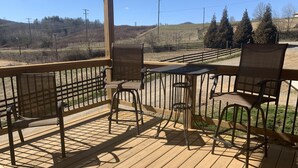 A wooden deck with metal chairs and a table, overlooking a hilly landscape with trees and power lines.