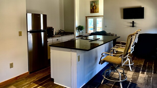 A modern kitchen with a large island, stainless steel refrigerator, and a dining area with a black couch and wicker chairs.