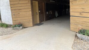A wooden building entrance with a door, a concrete pathway, and a small garden area with plants.
