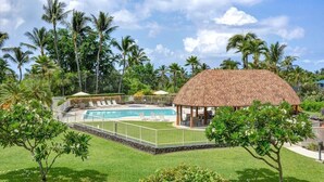 Ein Poolbereich mit einem strohgedeckten Pavillon, umgeben von Palmen und einem gepflegten Rasen.