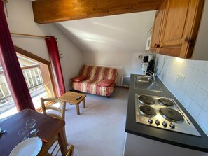 A compact kitchen with a stove, a dining table with chairs, and a sofa.