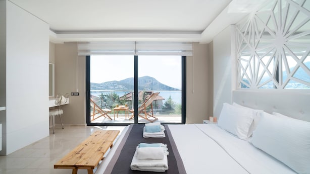 Une chambre d’hôtel moderne avec un grand lit, un banc en bois, une table avec des serviettes et une vue sur un lac et des montagnes.