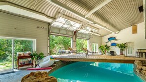An indoor swimming pool with a wooden deck, lounge chairs, and a view of greenery outside. - Large cottage with Water front, Heated Pool, sauna, 4 family rooms (Fergus)