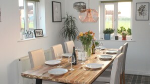 A dining area with a wooden table set for six, surrounded by chairs. There are potted plants on the windowsill, a hanging light fixture, and framed artwork on the walls. - Boasting a private garden, stunning views and ample parking. (St. Michael&rsquo;s on Wyre)