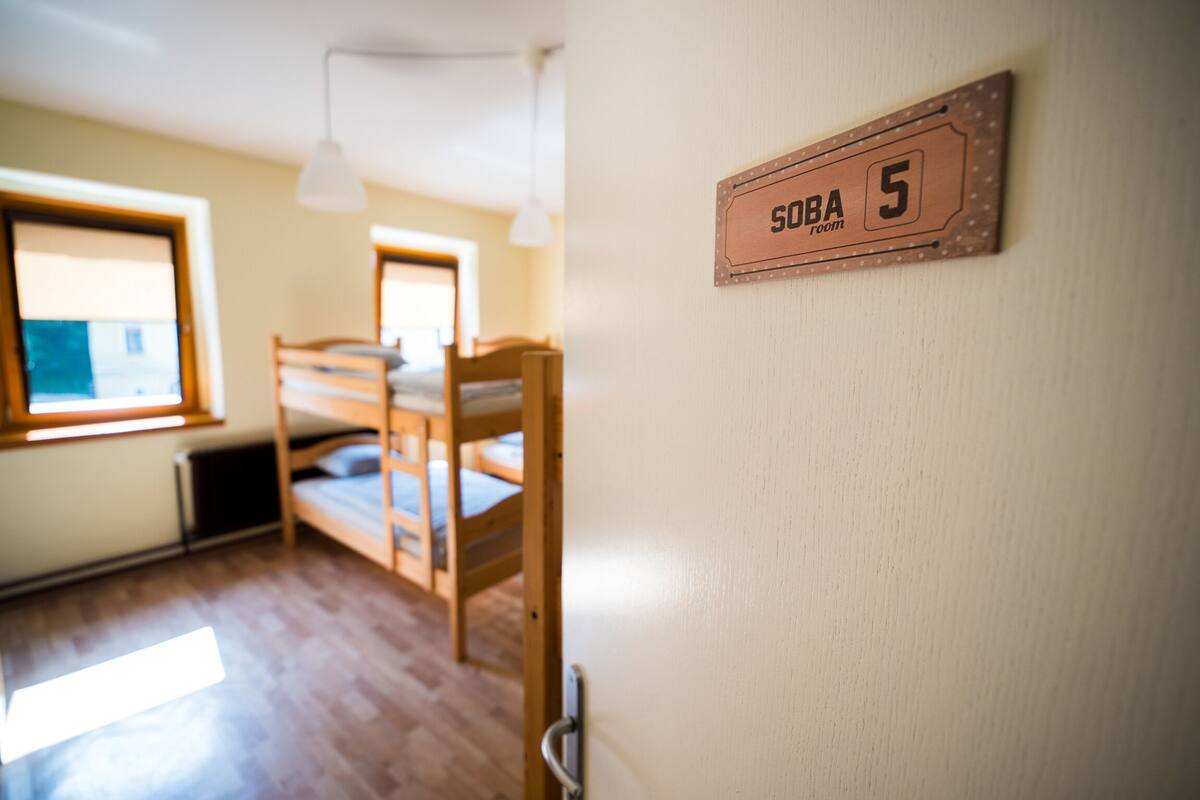 A dormitory room with bunk beds, a window, and a sign indicating 'SOBA room 5'.