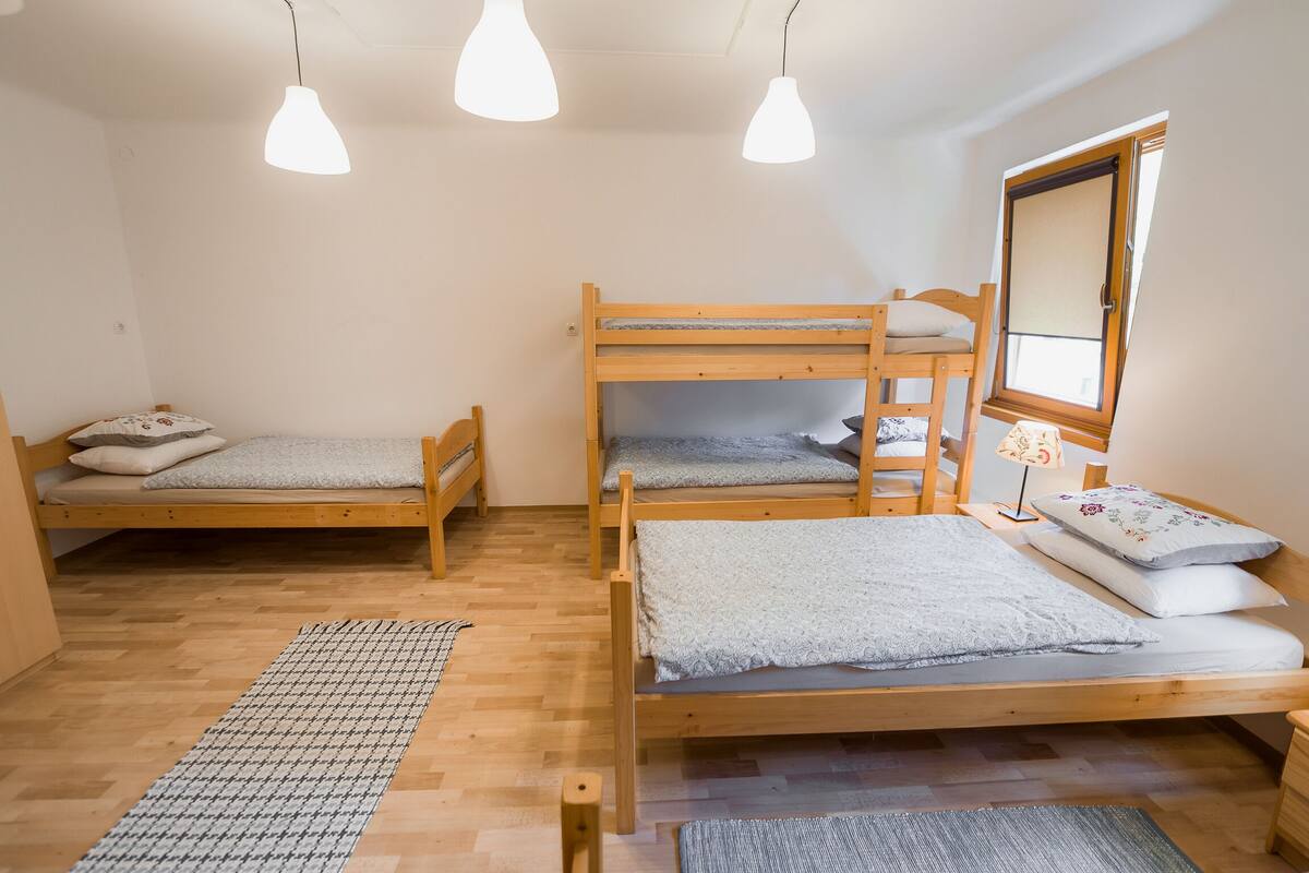 A dormitory room with three bunk beds, a window with a view, and pendant lights.