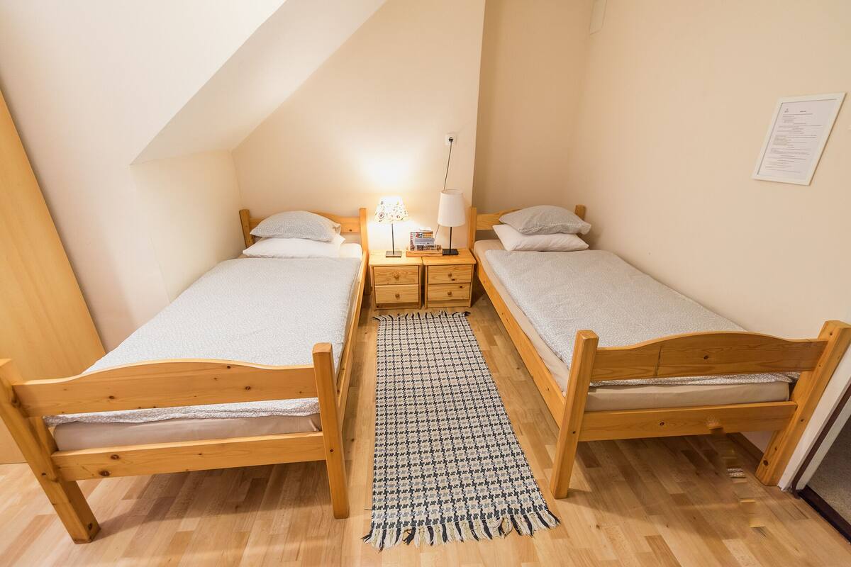 A small, cozy room with two wooden beds, a nightstand with a lamp, and a wooden floor.