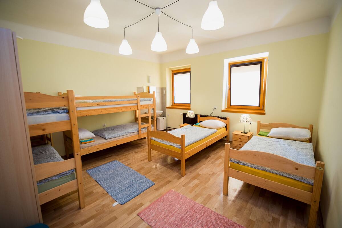 A dormitory room with bunk beds, a desk, a chair, and a window.