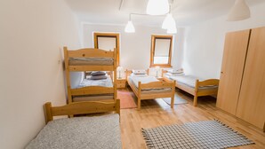 Un dormitorio con tres literas, un armario de madera y una pequeña mesa con una lámpara.