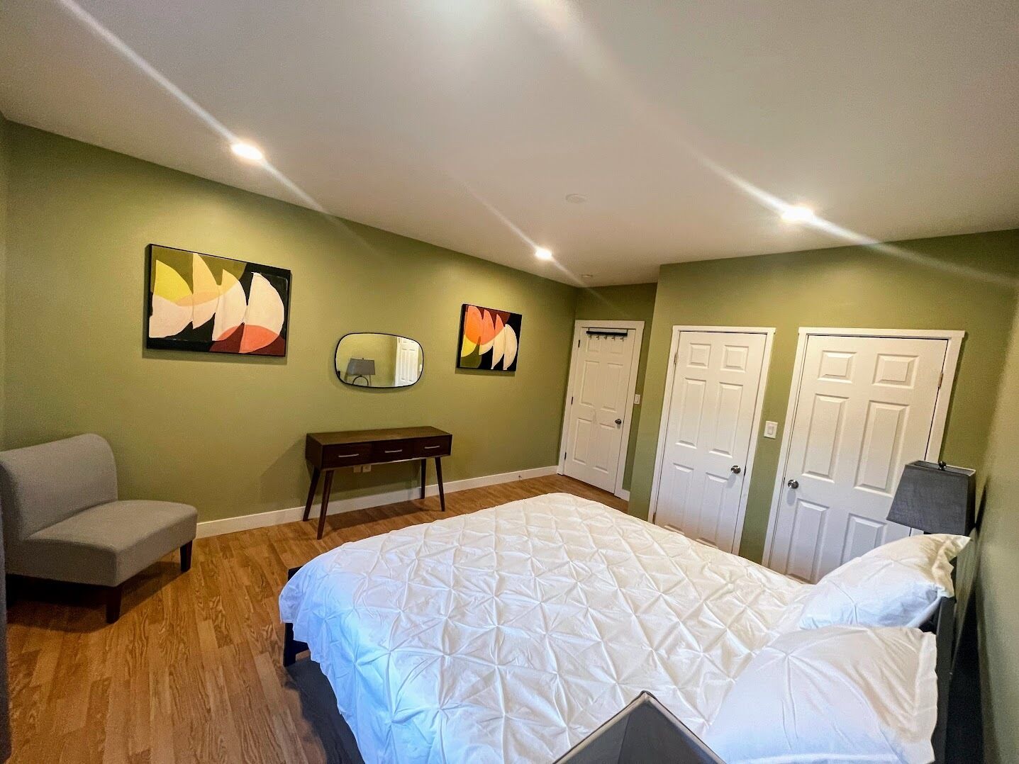 Un dormitorio con una cama, un banco, dos puertas y dos cuadros colgados en la pared.