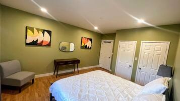 Un dormitorio con una cama, un banco, dos puertas y dos cuadros colgados en la pared.