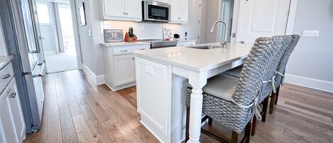 A modern kitchen with white cabinetry, a central island, and a dining area with wicker chairs.