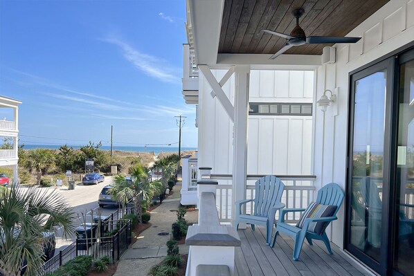 A coastal property with a wooden deck, two blue Adirondack chairs, and a view of the beach and ocean.
